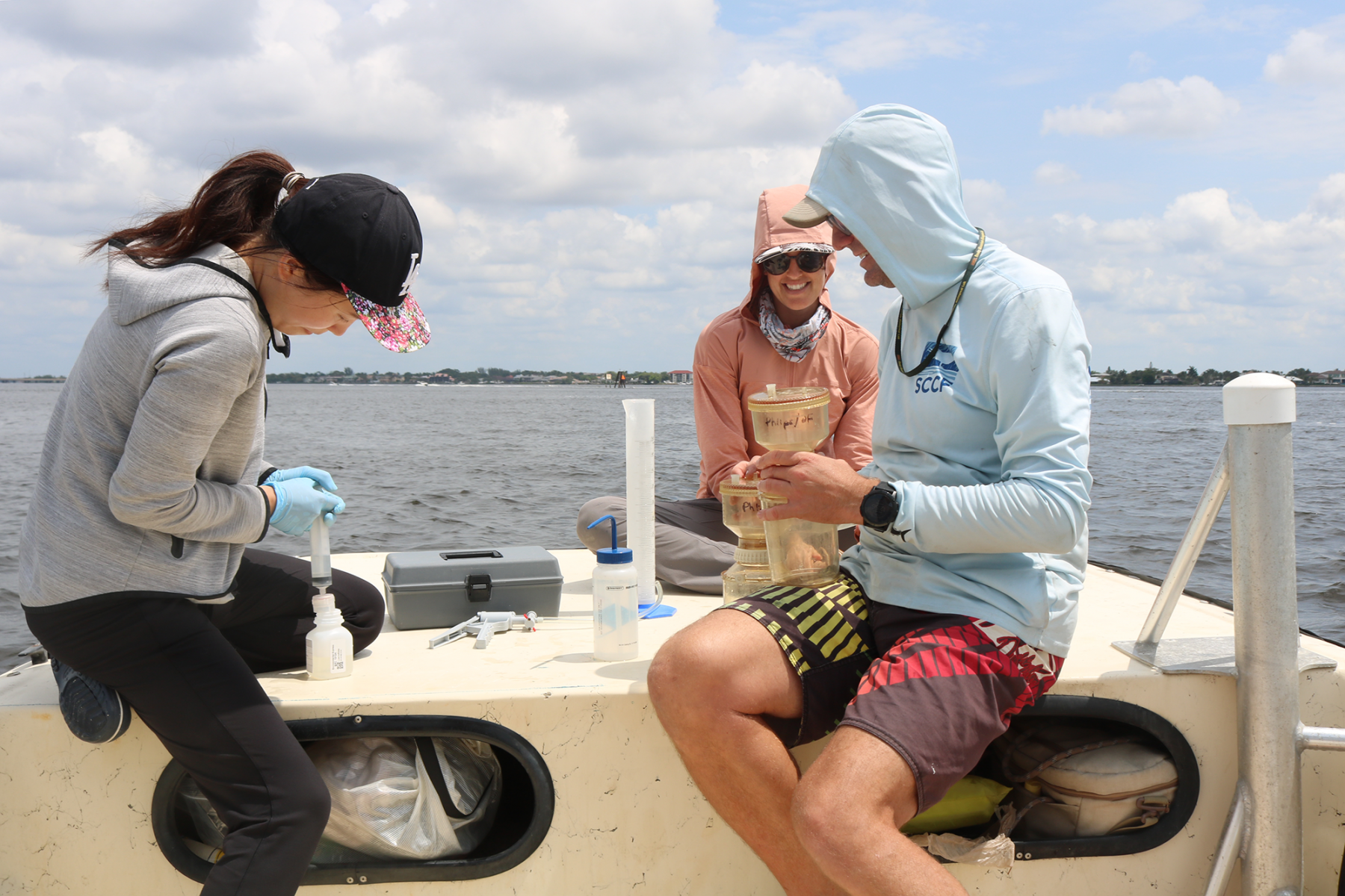 Three people sit on the bow of a boat using a collection of testing instruments.